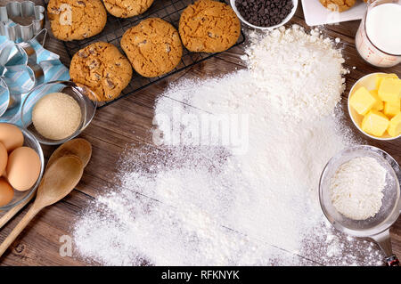 Frisch zubereitete Schokoladenkekse auf einem dunklen Holztisch mit Mehl bestäubt und Zutaten. Stockfoto