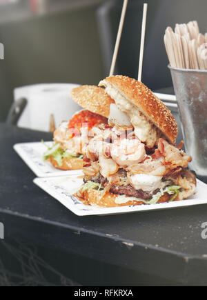 Street Food Burger mit Fisch, Speck, Fleisch, Gemüse und Mayonnaise. Street Food oder ungesundes Essen Konzept. Vintage tone Stockfoto