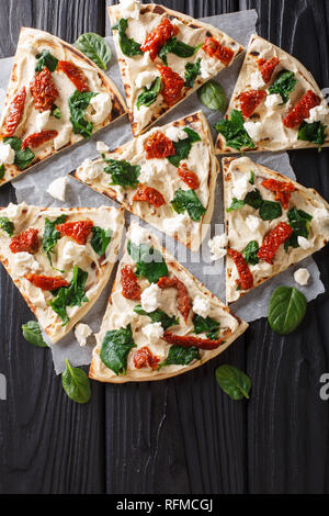 Fladenbrot mit Hummus, getrocknete Tomaten, Spinat und Ziegenkäse close-up auf dem Tisch. Senkrechte Draufsicht von oben Stockfoto