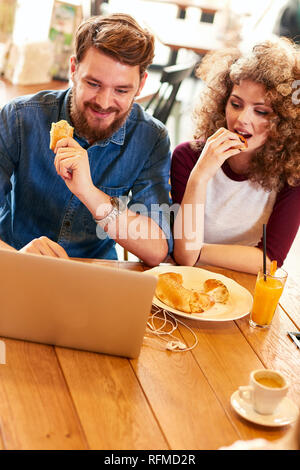 Männlichen und weiblichen Blick auf Laptop und Croissant Essen im Restaurant Stockfoto