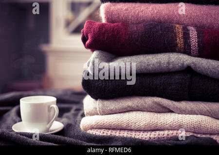 Stapel der bunten Pullover mit heißem Getränk weiße Tasse auf der Seite, den Hintergrund mit Kopie Raum, gemütliche hygge Tapete. Rosa Filter. Stockfoto