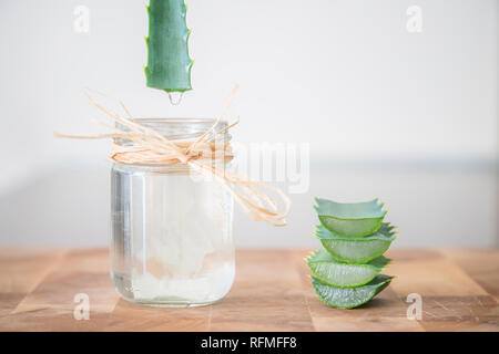 Essenz aus Aloe Vera Pflanze tropft in einen kosmetischen Flasche mit Schichten von Werk übereinander auf der Seite gestapelt Stockfoto