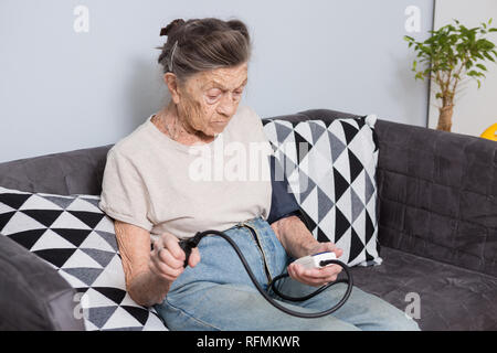 Das Thema ist sehr alte Person und gesundheitliche Probleme. Ein älterer kaukasische Frau, 90 Jahre alt, mit Falten und graue Haare, sitzt zu Hause auf dem Sofa und verwendet ein bl Stockfoto