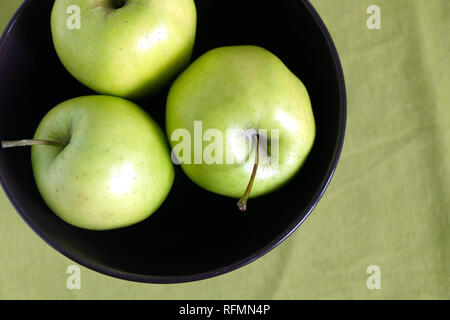 Drei grüne Äpfel innen lila Schüssel auf grün Tischdecke Draufsicht closeup Stockfoto