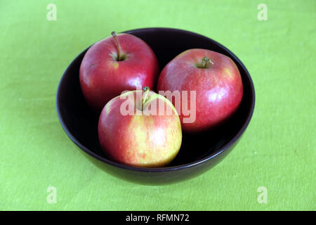 Drei rote Äpfel innen lila Schüssel auf grün Tischdecke Draufsicht closeup Stockfoto