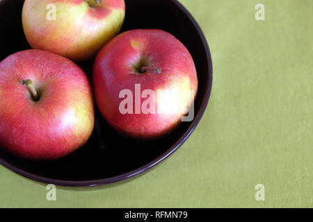 Drei rote Äpfel innen lila Schüssel auf grün Tischdecke Draufsicht closeup Stockfoto