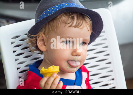 Das Porträt einer schönen jungen mit einem blauen Hut genießen Sie ein leckeres Eis. Er ist ein gelbes Eis in der Hand. Stockfoto