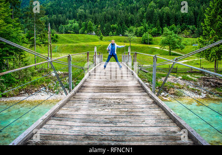 Gerne ferne Frau springen von einer hölzernen Fußgängerbrücke Fußgängerbrücke über den Fluss Soca in Slowenien in der wilden Natur Hintergrund Stockfoto