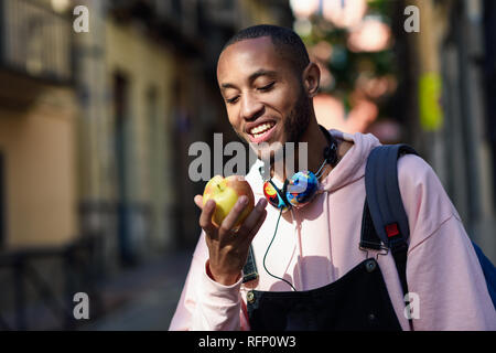 Junge schwarze Mann ißt einen Apfel auf der Straße. Lifestyle Konzept. Stockfoto