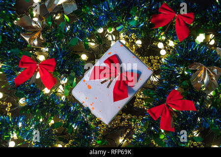 Verpackte Geschenk zwischen Weihnachten Lichter und bunten Dekorationen im Hintergrund Stockfoto
