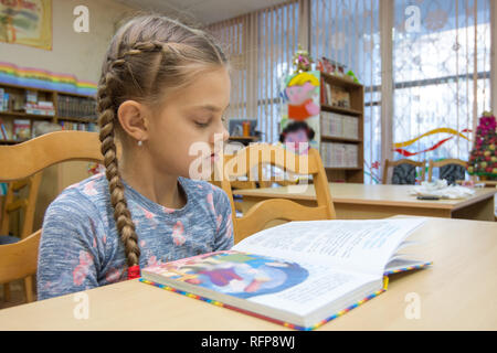 Ein Mädchen von zehn Jahre alt ist, ein Buch zu lesen in der Bibliothek Stockfoto