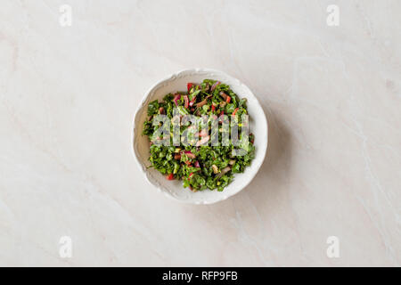 Gehackte Petersilie Salat mit Tomaten und Zwiebeln in Keramik Schüssel auf Marmor Oberfläche. Ökologische Lebensmittel. Stockfoto