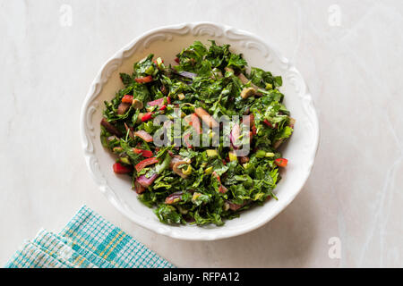 Gehackte Petersilie Salat mit Tomaten und Zwiebeln in Keramik Schüssel auf Marmor Oberfläche. Ökologische Lebensmittel. Stockfoto