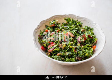 Gehackte Petersilie Salat mit Tomaten und Zwiebeln in Keramik Schüssel auf Marmor Oberfläche. Ökologische Lebensmittel. Stockfoto