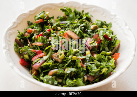 Gehackte Petersilie Salat mit Tomaten und Zwiebeln in Keramik Schüssel auf Marmor Oberfläche. Ökologische Lebensmittel. Stockfoto