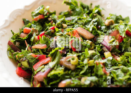 Gehackte Petersilie Salat mit Tomaten und Zwiebeln in Keramik Schüssel auf Marmor Oberfläche. Ökologische Lebensmittel. Stockfoto