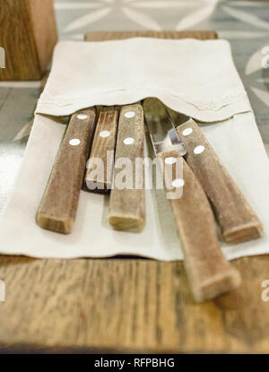 Besteck gewickelt in einem Leinen Servietten liegen auf einem Brot Teller auf einen hölzernen Tisch. Close Up, Low Angle. Stockfoto