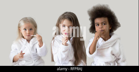 Drei Mädchen Freundinnen Lippenstift. Kinder verschiedener Nationalitäten in weißen Kitteln spielen mit dem Kometen der Eltern. Stockfoto