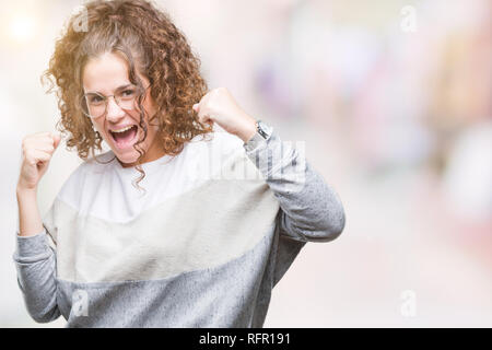 Schöne Brünette lockige Haare junge Mädchen Tragen einer Brille über isolierte Hintergrund sehr glücklich und aufgeregt, Sieger Geste mit erhobenen Armen, smilin Stockfoto