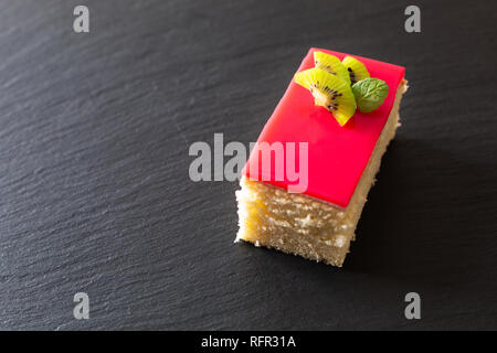 Hausgemachte organische Stück vanille Biskuit rote Beere Soße auf schwarzem Schiefer Stein Platte mit Kopie Raum Stockfoto