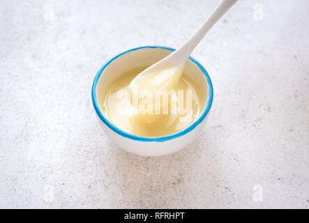 Kondensmilch in weiße Schüssel gießen. Süße vanille Sauce, kondensiert oder Kondensmilch, Ansicht von oben, kopieren. Stockfoto