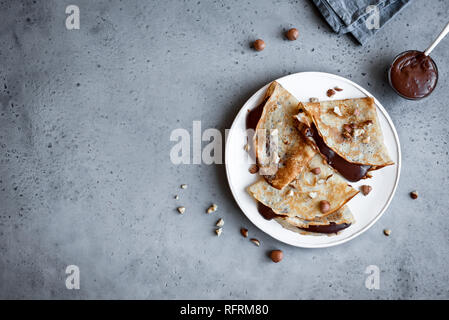 Pfannkuchen mit Nutella und Haselnüsse. Hausgemachte dünne Crepes für Frühstück oder Dessert auf rustikalen Hintergrund, kopieren. Stockfoto