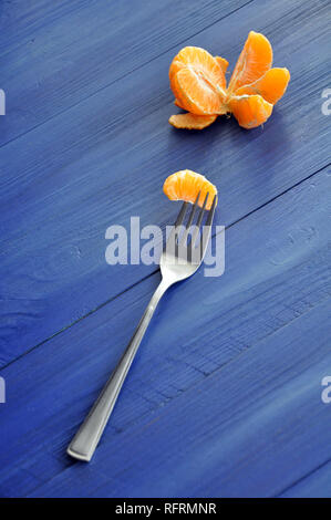 Geschälte Mandarine mit einem Slice auf der Gabel auf dem blauen Hintergrund Holz Stockfoto