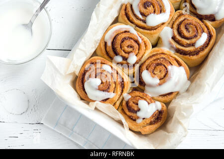 Zimtschnecken oder cinnabon, hausgemachtes Rezept des traditionellen Dessert süße Brötchen mit weiß Sahnesauce auf weißem Holz- Hintergrund. Stockfoto