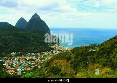 Einen herrlichen Blick auf den berühmten pitons Berge von St. Lucia, dominiert die umliegenden tropischen Landschaft, in der Nähe ein Dorf an der Küste. Stockfoto