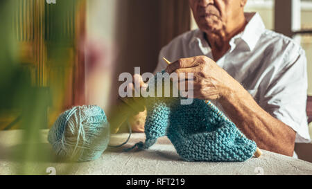 Der alte Mann die Hände stricken mit Nadeln und Wolle Garn. Pensionierter mann Stricken zu Hause. Stockfoto