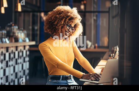 Weibliche Unternehmer arbeiten am Laptop sitzen in einem Restaurant und Musik zu hören. Lächelnd afro-amerikanische Frau an einem Cafe mit Ihrem Laptop. Stockfoto