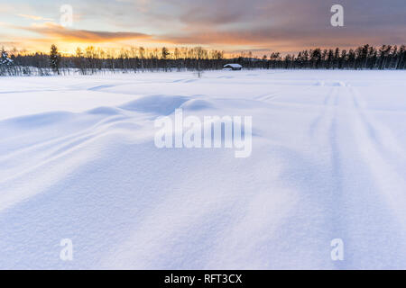 Winter Sonnenuntergang im finnischen Lappland mit Hütte und Wald im Hintergrund, tiefen Schnee im Vordergrund. Bild in Pyha, Finnland. Stockfoto