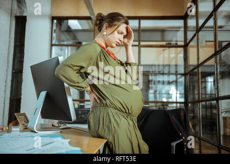 Dunkelhaarige schwangere Frau tragen khaki Kleid in Kopfschmerzen Stockfoto