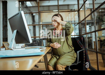 Schwangere Frau sitzt im Büro Gefühl schrecklich und besorgt Stockfoto