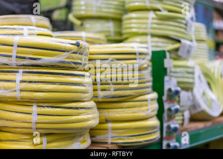 Stapel von Rollen gelb pvc Rohr auf der Theke im Store. Verkauf Schläuche in den Garten von verschiedenen Herstellern, in den Regalen zu speichern. Schlauch für Stockfoto