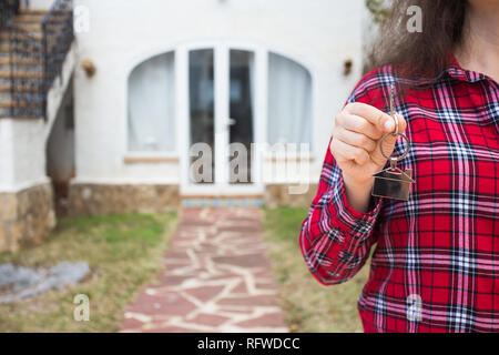 Immobilien und Grundstücke Konzept - Nahaufnahme von Frau mit Haus Tasten auf Haus geformte Schlüsselbund vor ein neues Zuhause. Stockfoto