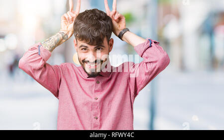 Jungen gutaussehenden Mann mit rosa Shirt über isolierte Hintergrund posiert lustige und verrückte mit den Fingern auf dem Kopf wie Hasenohren, lächelt Fröhlich Stockfoto