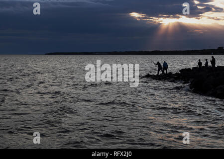 Eine Silhouette einer Gruppe von Fischern auf den Felsen in den Sonnenuntergang - Summerside, Prince Edward Island, Kanada Stockfoto