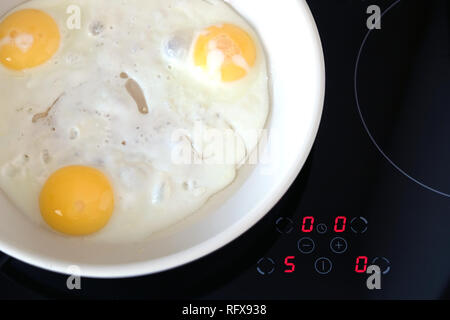 Bereit Frühstück am Herd. Drei leckere Spiegeleier in der weißen Wanne auf moderne Küche E-Herd mit elektronischem Bedienfeld Ansicht von oben closeup Stockfoto