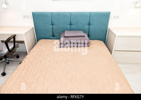 Hotel Bett mit Kopfteil und Grün Blau Büro Stuhl Tisch Schreibtisch mit Lampe kissen im Schlafzimmer im Haus oder Apartment mit Blätter und dresse Stockfoto