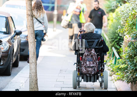 London, Großbritannien - 13 September, 2018: die Menschen auf der Straße auf der Straße gehsteig Bürgersteig in Chelsea oder Belgravia mit einem behinderten älteren Mann oder Frau reiten auf wh Stockfoto