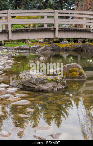 Iew von bemoosten Felsen und koi Teich mit gewölbten Brücke an Kasugai Gärten, einen japanischen Garten im Zentrum von Kelowna, British Columbia, Kanada Stockfoto