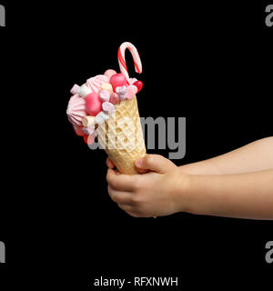 Leckere Süßigkeiten in Form einer Waffel Kegel mit Süßigkeiten, Eibisch und Lutscher in der Hand des Kindes auf einem schwarzen Hintergrund gefüllt Stockfoto