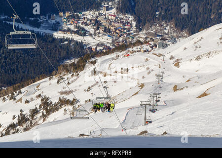 Die Leute steigen mit dem Skilift auf dem Hintergrund der Stadt Dombai Winter sonniger Tag Stockfoto