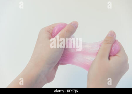 Ziehen rosa Schleim in die Hände, rote klebrige Plastilin Stockfoto