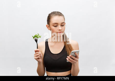 Schöne junge Frau tragen Sportliche Kleidung mit Salat in der Hand, mittels Smart Phone. Stockfoto