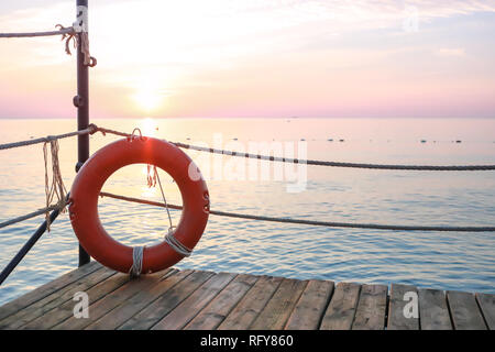 Rot Rettungsring auf hölzernen Pier auf Hintergrund der Marine in der Morgendämmerung. Stockfoto