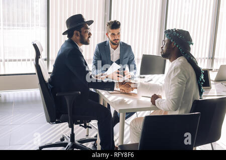 Versiegelung ist ein Deal. Blick von oben auf die drei Männer am Schreibtisch sitzen und die Hände schütteln Stockfoto