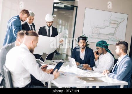 Multiethnische Gruppe von Bauherren und Architekten diskutieren Blueprint im Büro. Stockfoto