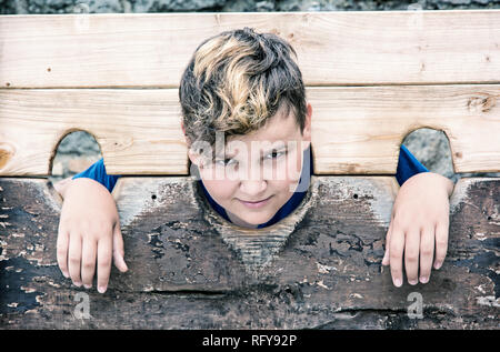 Jungen kaukasischen Jungen in mittelalterlichen Pranger. Elend Thema. Strafe Gerät. Blau Foto Filter. Stockfoto